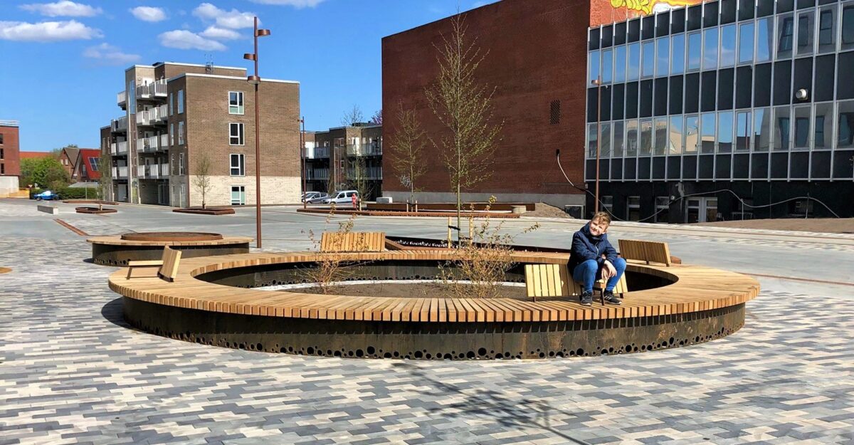 cirkelbænke i cortenstål beklædt med træ, med rygstøtte og specialdesignede huller i bunden, der er lavet til at lade regnvandet gå igennem og vande planterne