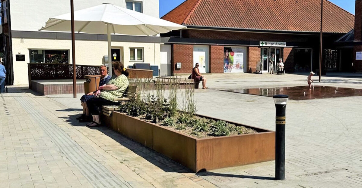 en cortenstål plantekasse med bænk beklædt med mahogni træ monteret på den på Ringe Torv