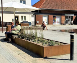 en cortenstål plantekasse med bænk beklædt med mahogni træ monteret på den på Ringe Torv