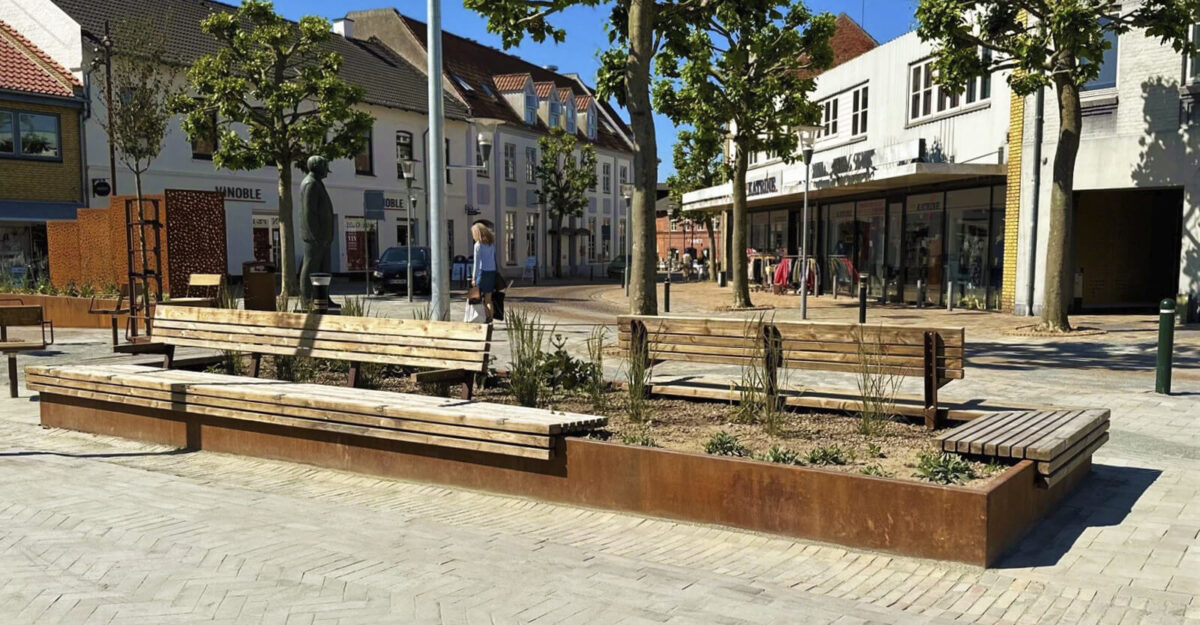 en cortenstål plantekasse med bænk beklædt med mahogni træ monteret på den på Ringe Torv