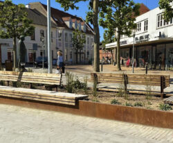 en cortenstål plantekasse med bænk beklædt med mahogni træ monteret på den på Ringe Torv