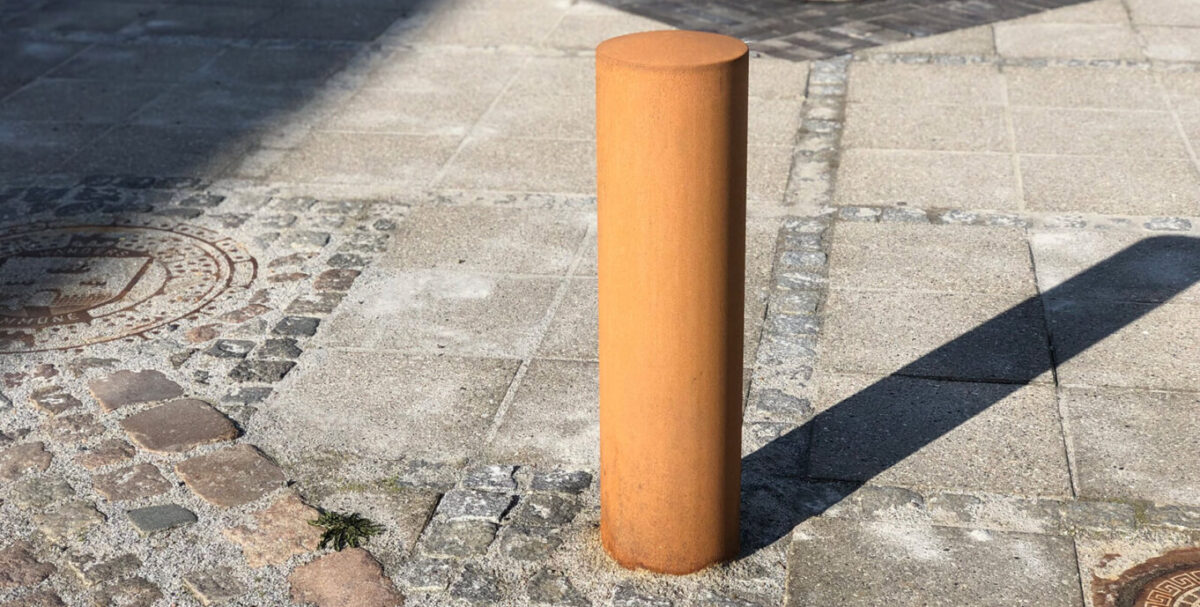 stor rund corten pullert nedstøbt på gaden i Langå