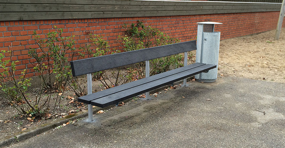 en lange udendørs bænk i galvaniseret stål og beklædt med genbrugsplast planker samt en affaldsbeholder i strækmetal